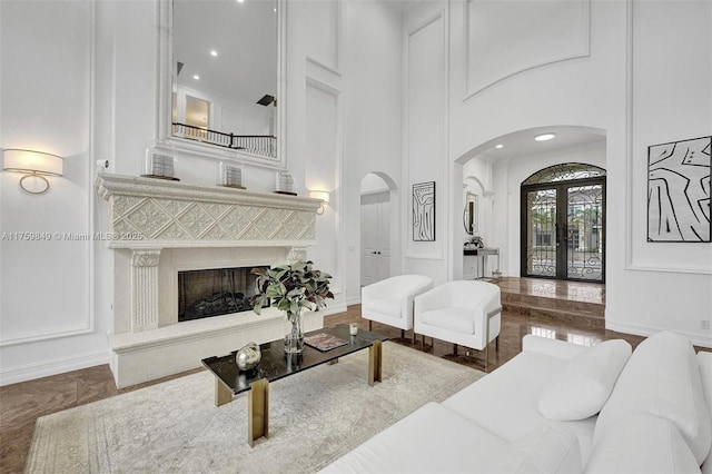 living area with a premium fireplace, a high ceiling, arched walkways, french doors, and a decorative wall