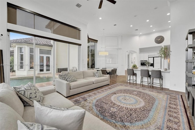 living room with visible vents, a ceiling fan, recessed lighting, arched walkways, and a high ceiling