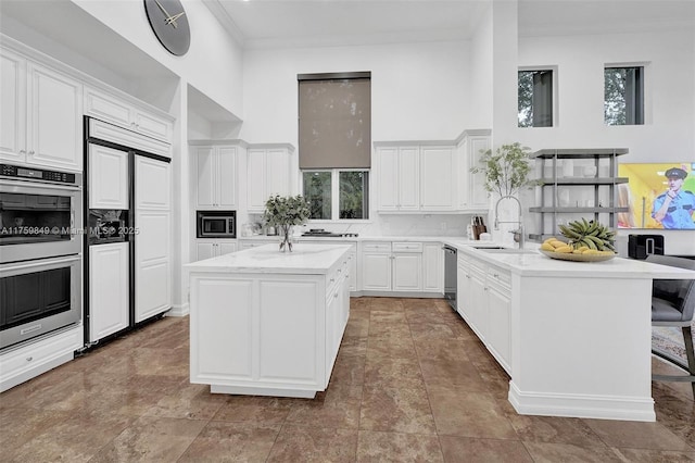 kitchen with a sink, built in appliances, white cabinetry, crown molding, and a center island