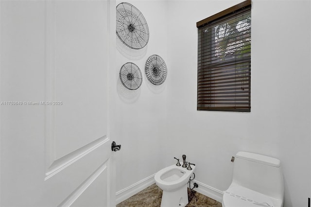 bathroom featuring toilet, a bidet, and baseboards