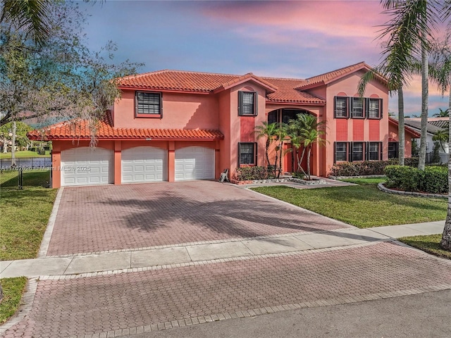 mediterranean / spanish house featuring stucco siding, a tiled roof, decorative driveway, and a front lawn