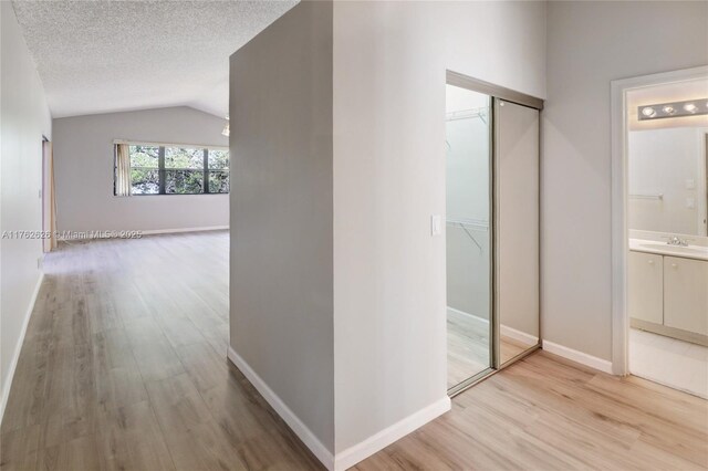 221 NW 201st Ave, Pembroke Pines, FL 33029 - hallway with light wood finished floors, lofted ceiling, a sink, baseboards, and a textured ceiling