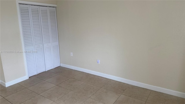 unfurnished bedroom featuring a closet, light tile patterned floors, and baseboards