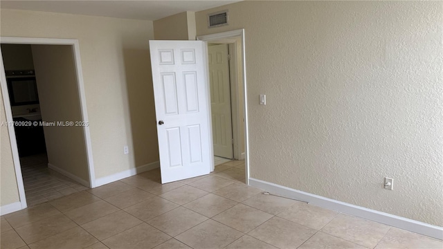 unfurnished bedroom featuring light tile patterned flooring, baseboards, visible vents, and a textured wall