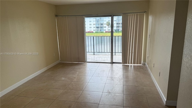 empty room with tile patterned floors, a textured wall, baseboards, and a water view