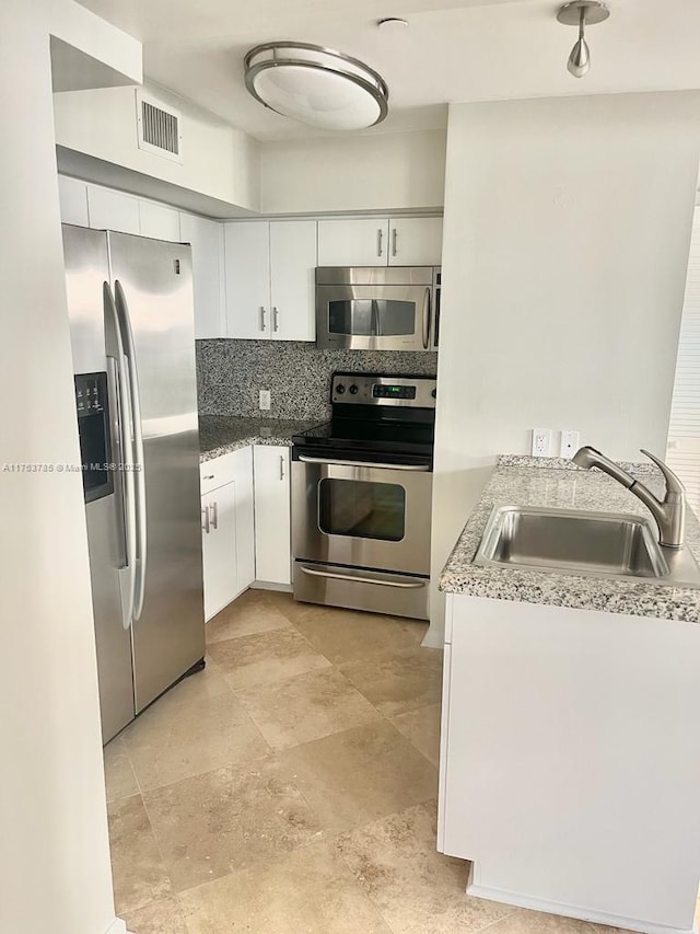 kitchen with visible vents, a sink, stainless steel appliances, white cabinetry, and tasteful backsplash