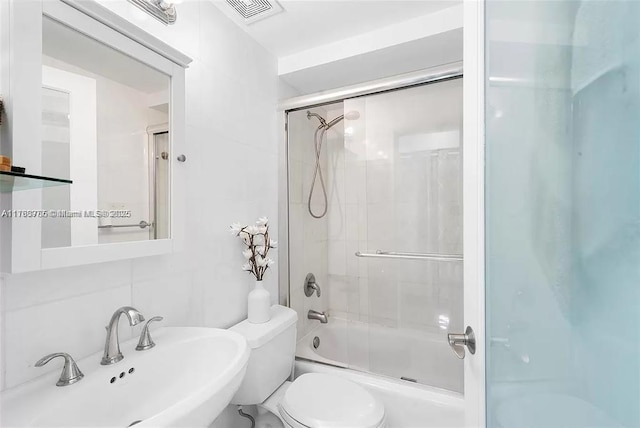 full bathroom featuring visible vents, toilet, combined bath / shower with glass door, tile walls, and a sink