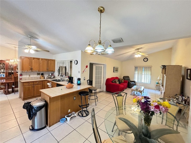 kitchen with visible vents, ceiling fan with notable chandelier, a sink, lofted ceiling, and tile counters