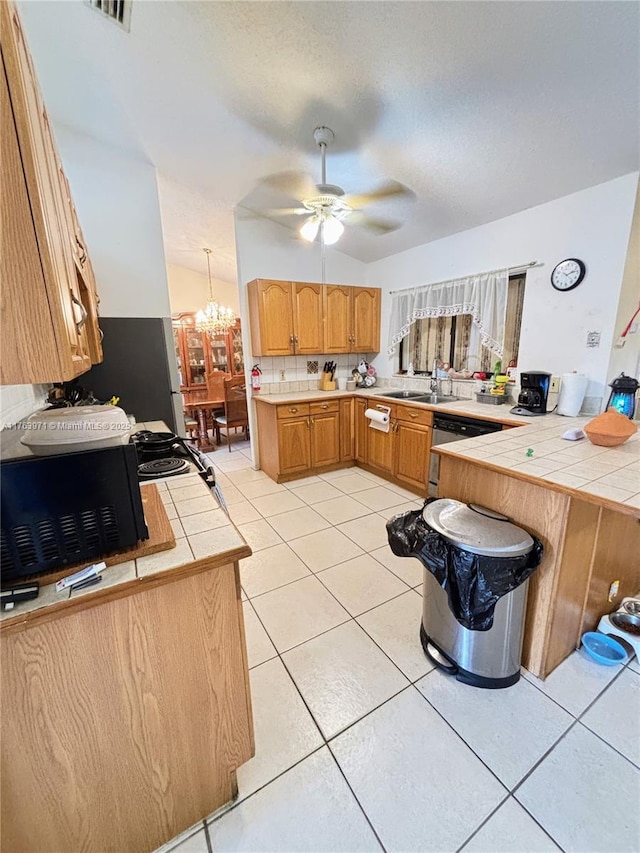 kitchen featuring tile countertops, a peninsula, light tile patterned flooring, a sink, and ceiling fan with notable chandelier