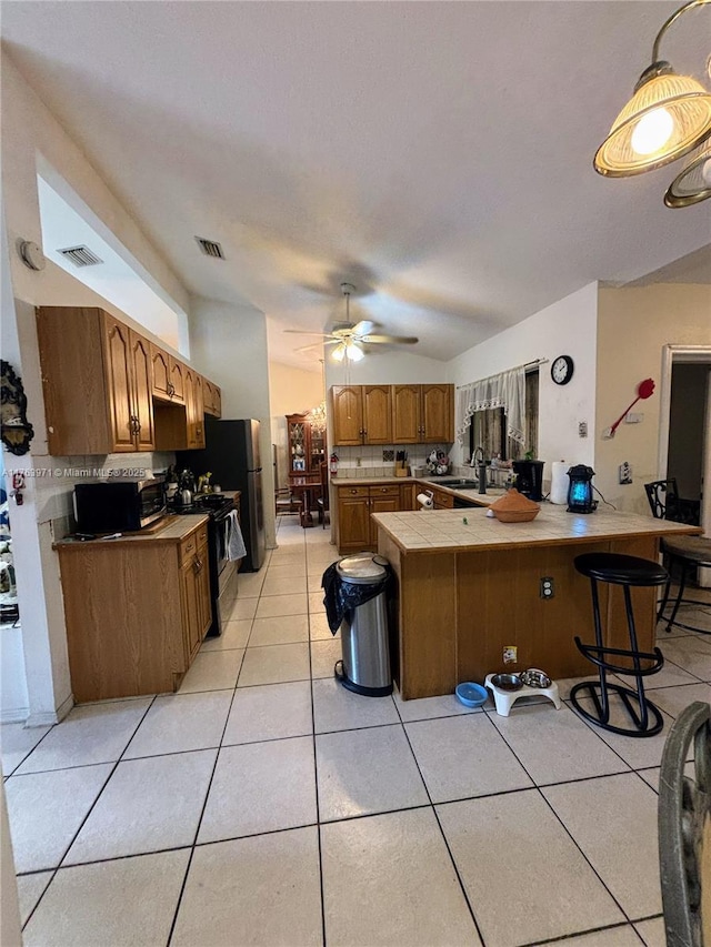 kitchen featuring visible vents, tile countertops, a peninsula, light tile patterned flooring, and black range with gas stovetop