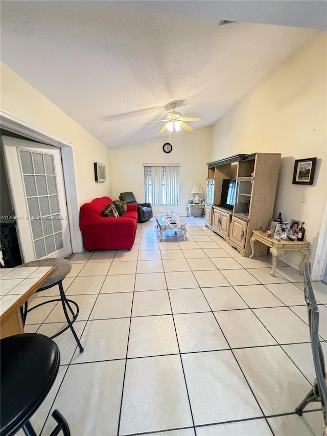 living area featuring vaulted ceiling, light tile patterned floors, a ceiling fan, and a textured ceiling