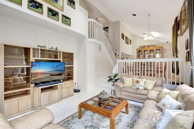 living area featuring stairway, light tile patterned floors, visible vents, a high ceiling, and a notable chandelier