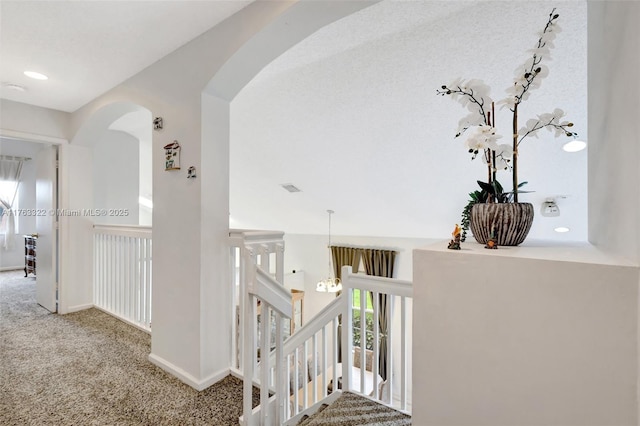 hallway with arched walkways, an upstairs landing, baseboards, and carpet floors