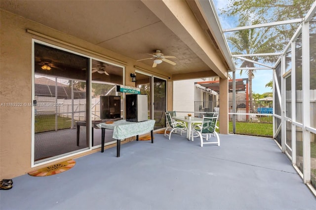 view of patio / terrace featuring a lanai, outdoor dining space, ceiling fan, and fence