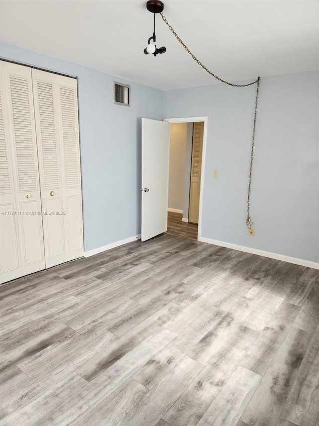 unfurnished bedroom featuring a closet, visible vents, baseboards, and wood finished floors