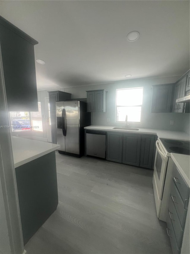 kitchen with light wood-style flooring, a sink, light countertops, stainless steel fridge, and white range with electric stovetop