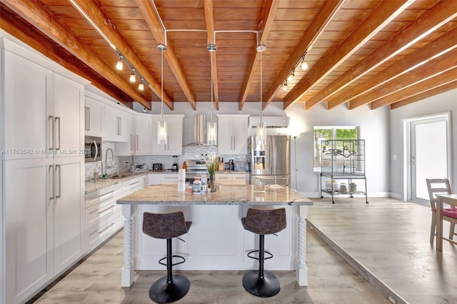 kitchen featuring a kitchen island, wall chimney range hood, decorative backsplash, stainless steel appliances, and a sink