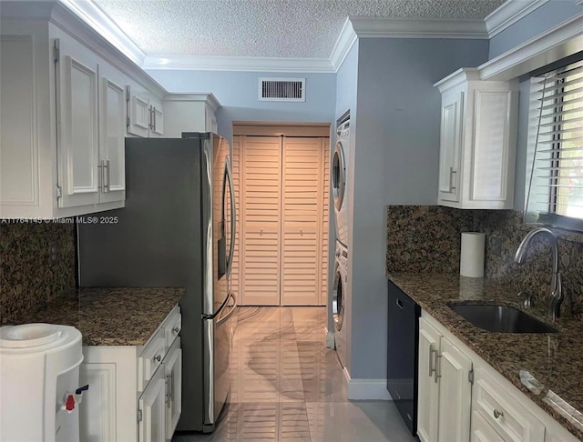 kitchen featuring a sink, visible vents, stacked washer and clothes dryer, and white cabinetry