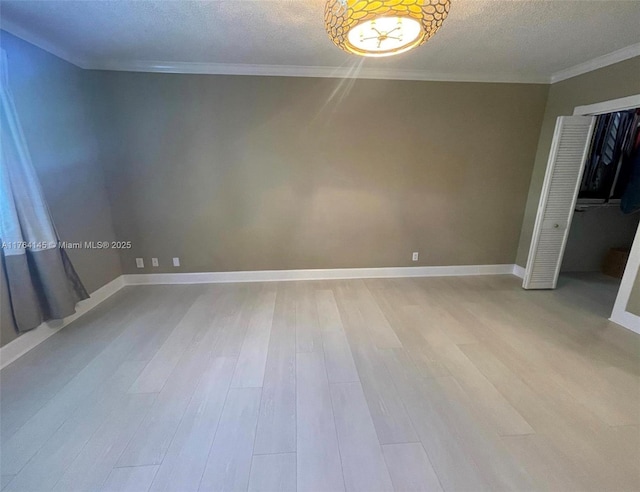 empty room with a textured ceiling, baseboards, light wood finished floors, and ornamental molding