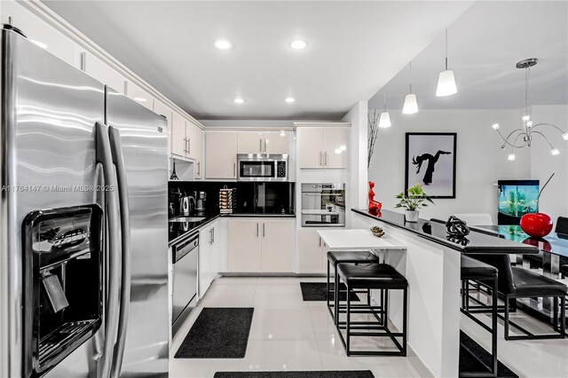 19380 Collins Ave Unit 307, Sunny Isles Beach, FL 33160 - kitchen with appliances with stainless steel finishes, a breakfast bar area, white cabinets, an inviting chandelier, and light tile patterned floors