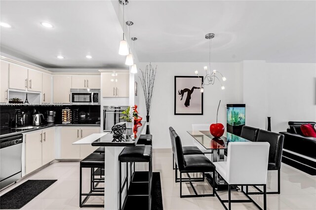19380 Collins Ave Unit 307, Sunny Isles Beach, FL 33160 - kitchen featuring a notable chandelier, a breakfast bar, dark countertops, appliances with stainless steel finishes, and white cabinets