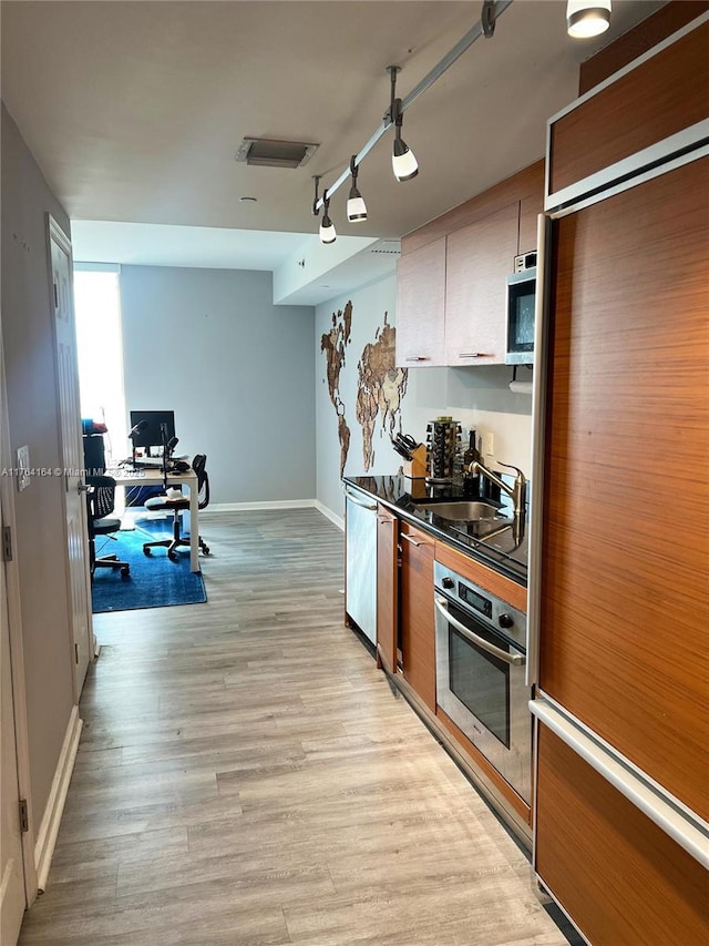 kitchen featuring baseboards, light wood finished floors, a sink, rail lighting, and appliances with stainless steel finishes