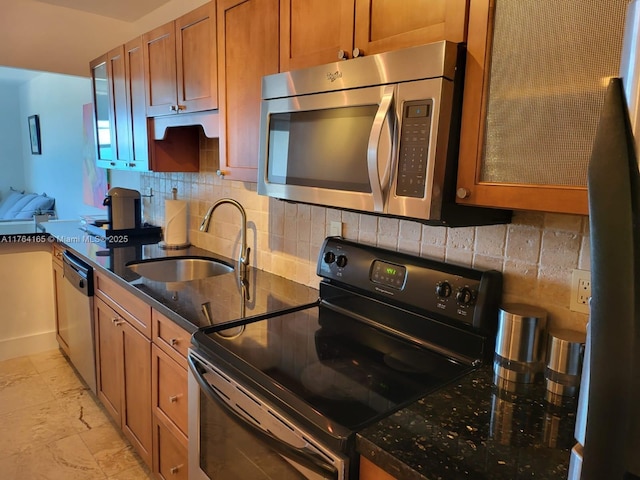 kitchen featuring backsplash, dark stone countertops, brown cabinetry, stainless steel appliances, and a sink