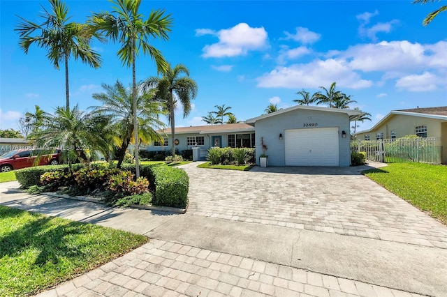 ranch-style house with decorative driveway, a front lawn, an attached garage, and fence