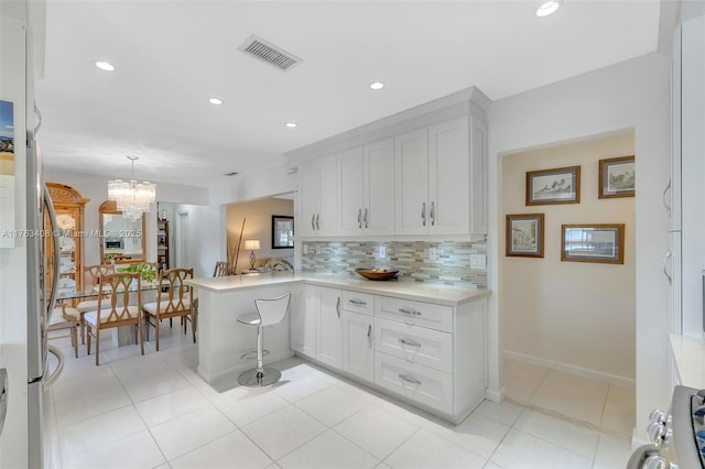 kitchen featuring tasteful backsplash, visible vents, light countertops, a peninsula, and a notable chandelier