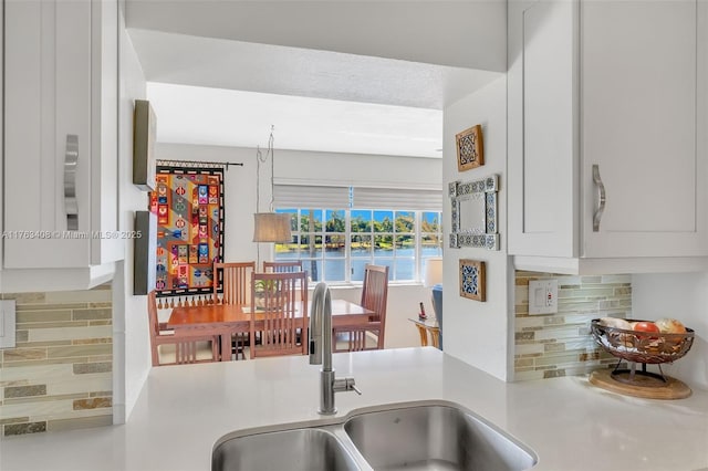 kitchen with backsplash, white cabinetry, light countertops, and a sink