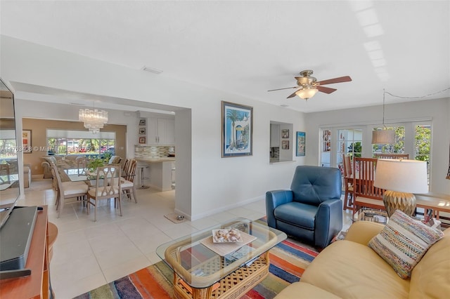 living room featuring light tile patterned floors, ceiling fan with notable chandelier, and baseboards