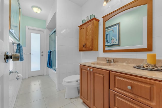 bathroom featuring tile patterned flooring, toilet, vanity, combined bath / shower with glass door, and tile walls