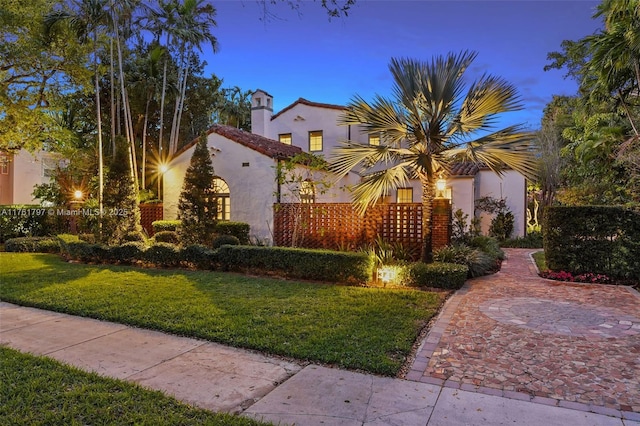 mediterranean / spanish house featuring a front lawn, a tile roof, and stucco siding