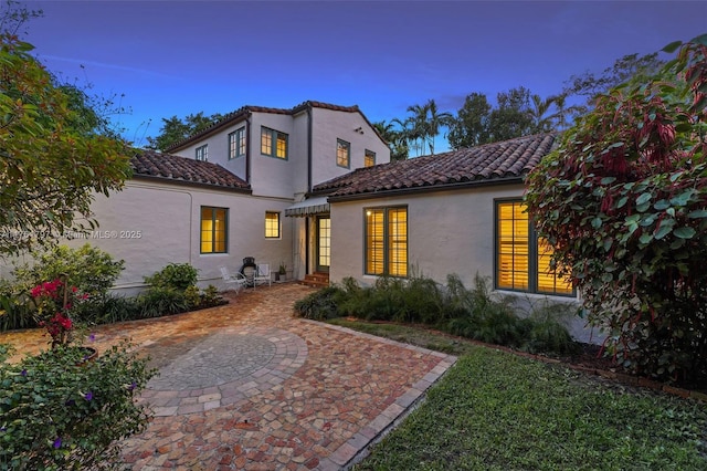 back of house featuring a tiled roof and stucco siding