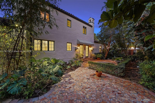 view of front of property featuring stucco siding, a chimney, and a tile roof