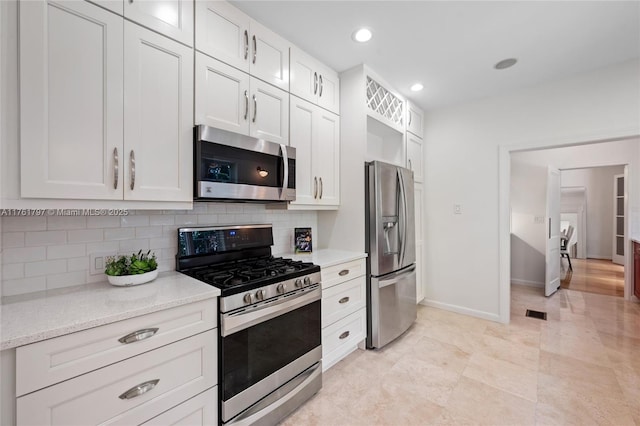 kitchen featuring light stone counters, appliances with stainless steel finishes, white cabinets, decorative backsplash, and baseboards