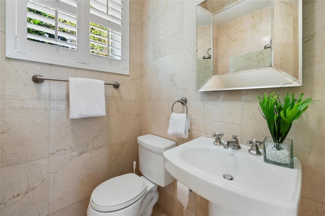 bathroom with a sink, toilet, and tile walls