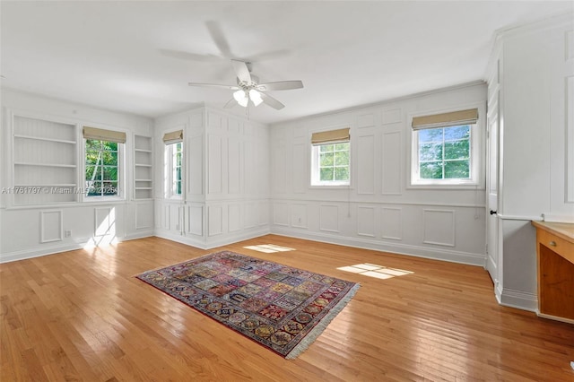 spare room featuring built in features, light wood-style flooring, and a decorative wall