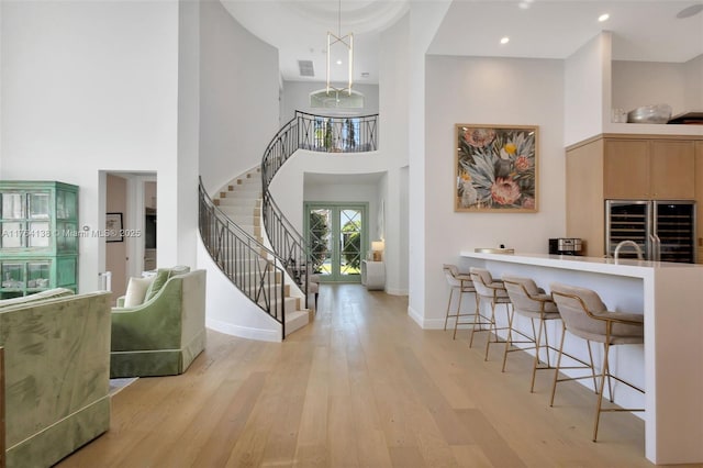 entrance foyer with light wood finished floors, visible vents, baseboards, stairs, and a towering ceiling