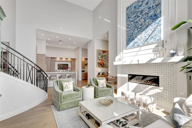 living room with a fireplace, recessed lighting, stairs, light wood-style floors, and a towering ceiling