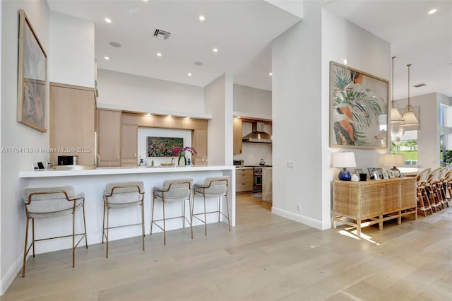 kitchen featuring high end range, visible vents, light wood finished floors, a kitchen bar, and wall chimney exhaust hood