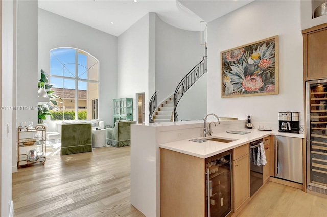 kitchen featuring wine cooler, light wood-style flooring, a peninsula, a towering ceiling, and a sink