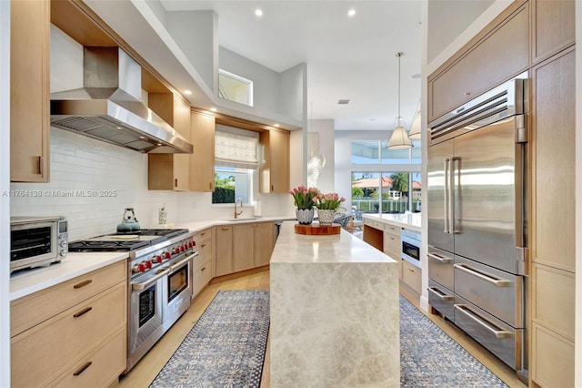 kitchen featuring backsplash, light brown cabinetry, premium appliances, wall chimney exhaust hood, and a sink