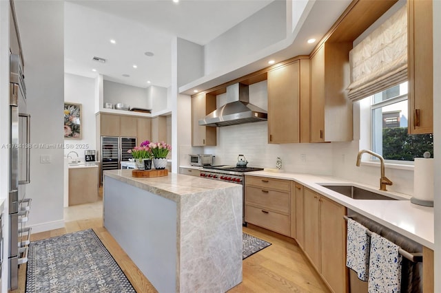 kitchen with a center island, wall chimney range hood, light brown cabinetry, high end stainless steel range oven, and a sink