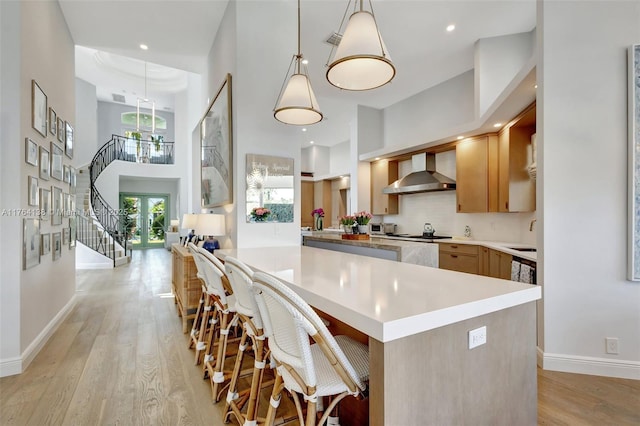 kitchen with decorative backsplash, light countertops, light wood-style floors, a towering ceiling, and wall chimney range hood