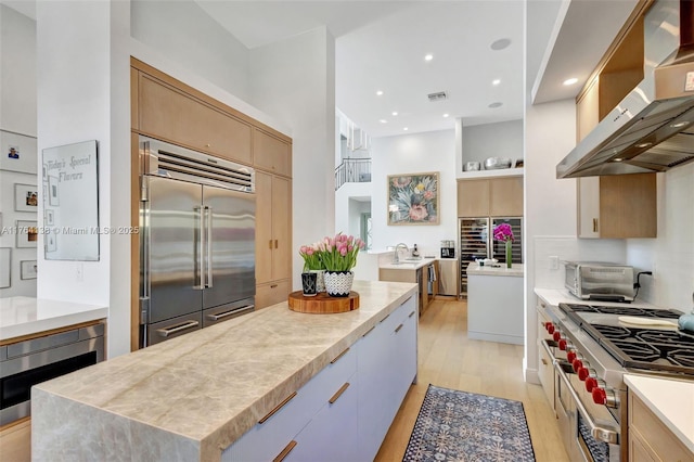 kitchen with a toaster, built in appliances, light countertops, range hood, and light wood-style flooring