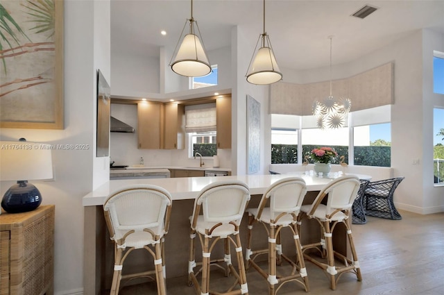 kitchen featuring visible vents, a sink, light countertops, light wood-style floors, and wall chimney range hood