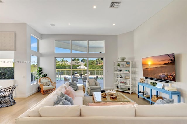 living area with visible vents, wood finished floors, recessed lighting, baseboards, and a towering ceiling