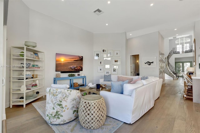 living room featuring visible vents, light wood finished floors, a high ceiling, and stairway