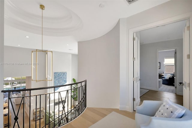 corridor with a raised ceiling, recessed lighting, wood finished floors, and an upstairs landing